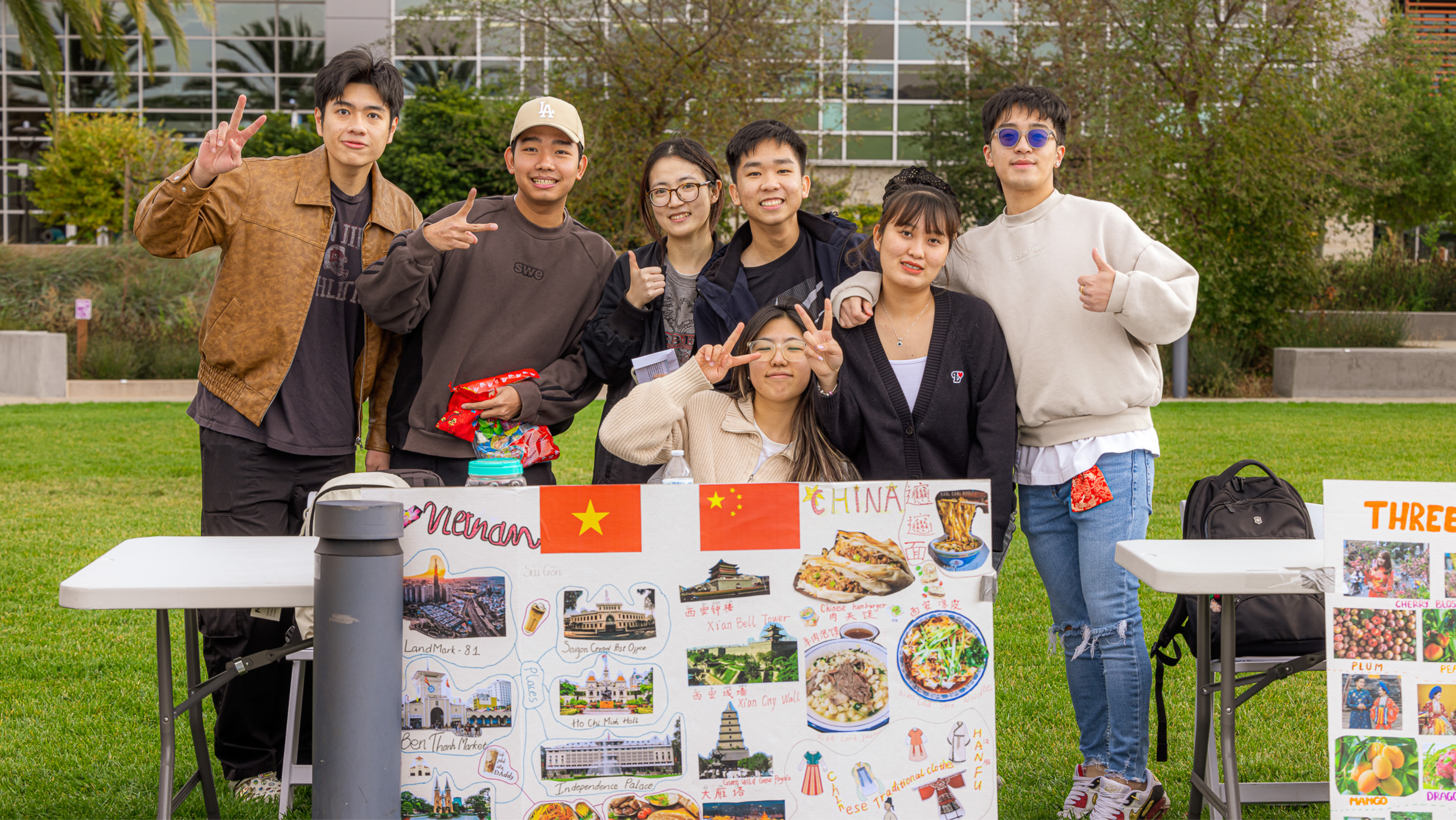 tudents posing outdoors behind a poster board displaying cultural landmarks and traditions from Vietnam and China.