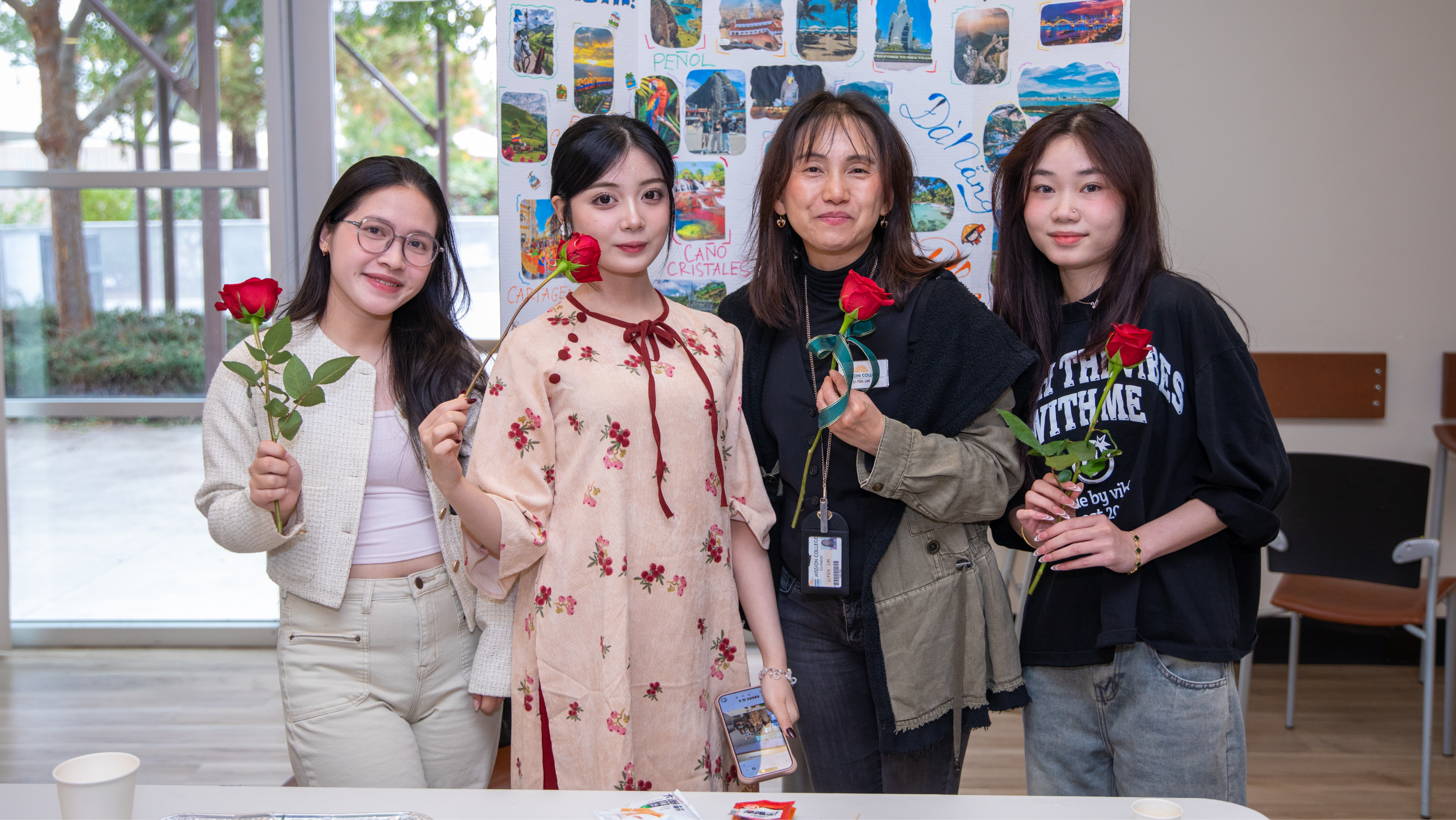 Four students and staff members holding red roses and smiling together at a campus reception.