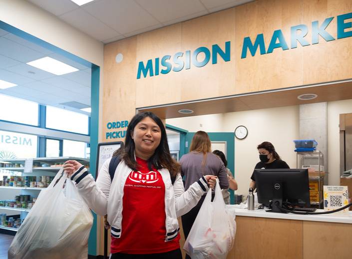 Young woman holds two bags of groceries as she exits the Mission Market.