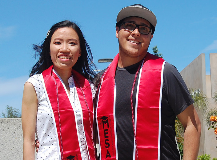 A young man and young woman pose together in bright red MESA sashes at commencement. 
