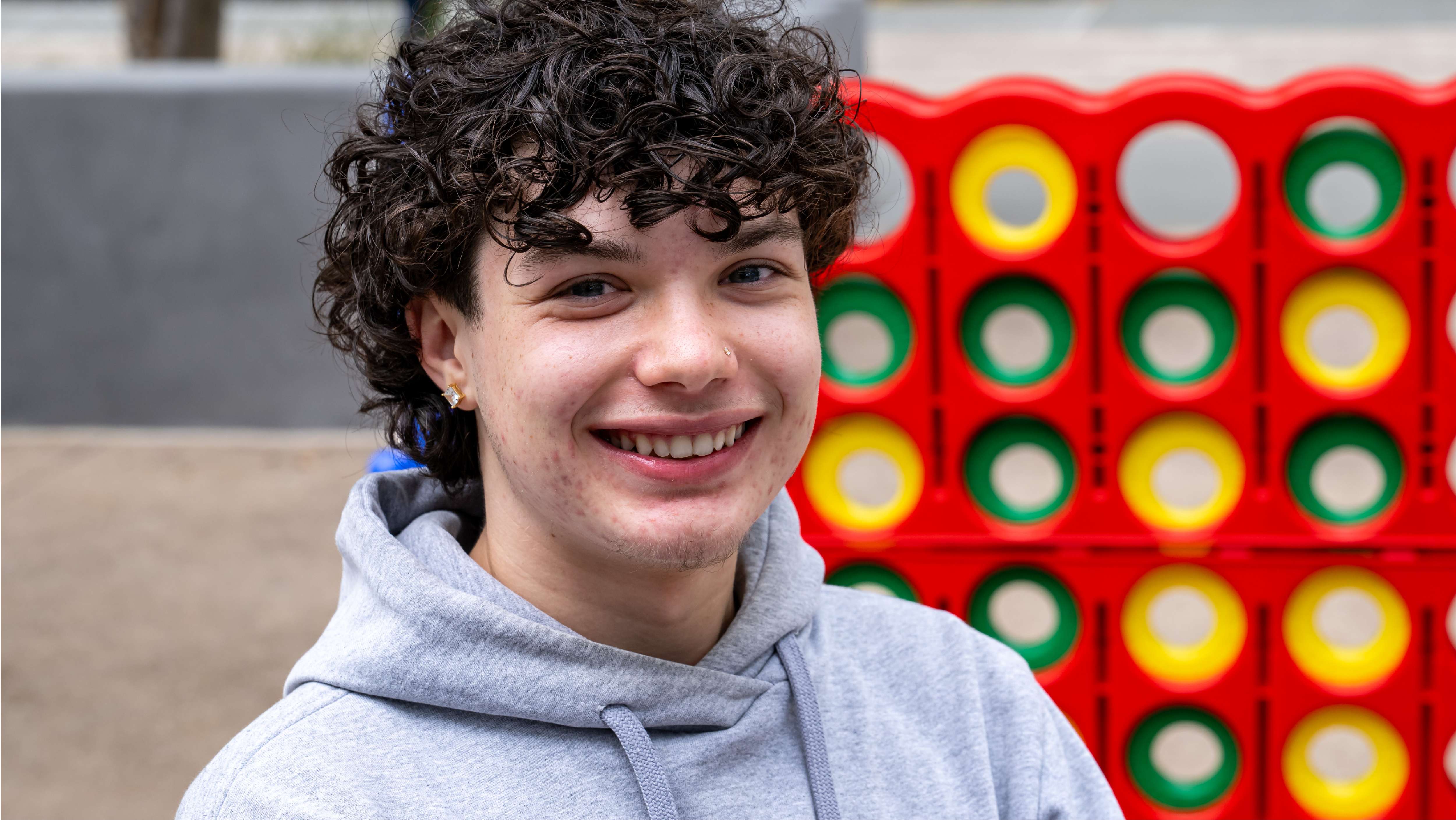 A smiling student in a grey hoodie posed in front of a giant lawn game on campus.