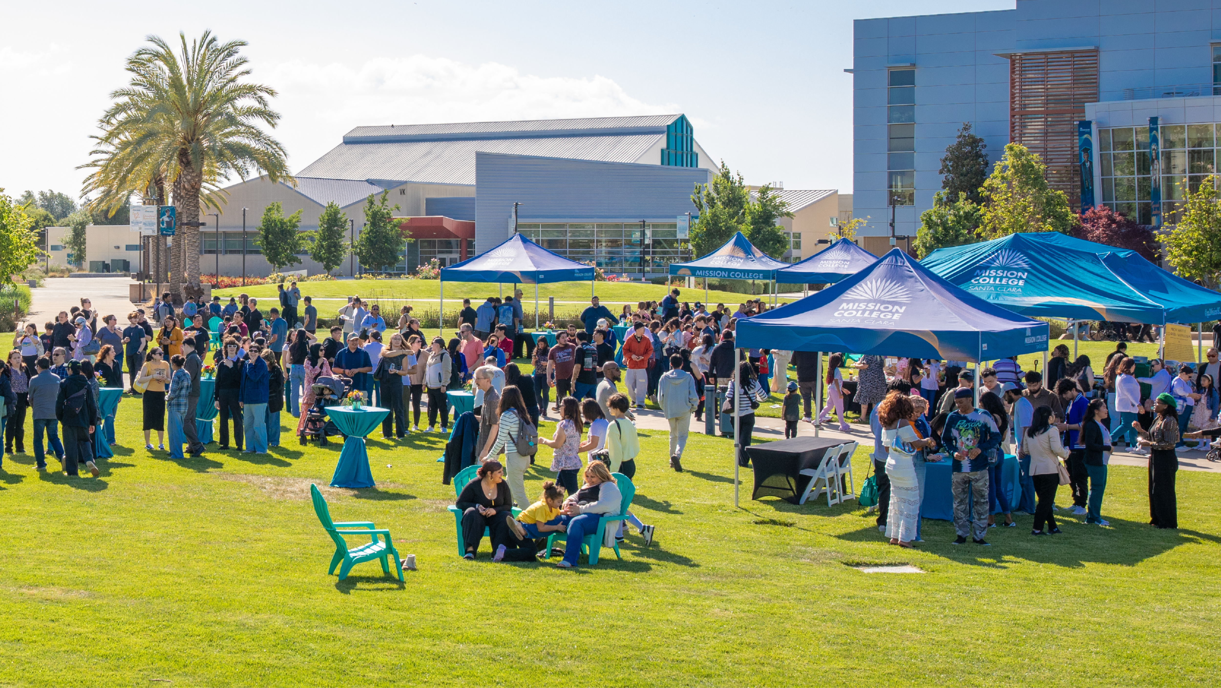 A wide outdoor shot of a bustling campus event with blue tents, information tables, and crowds on the central lawn.