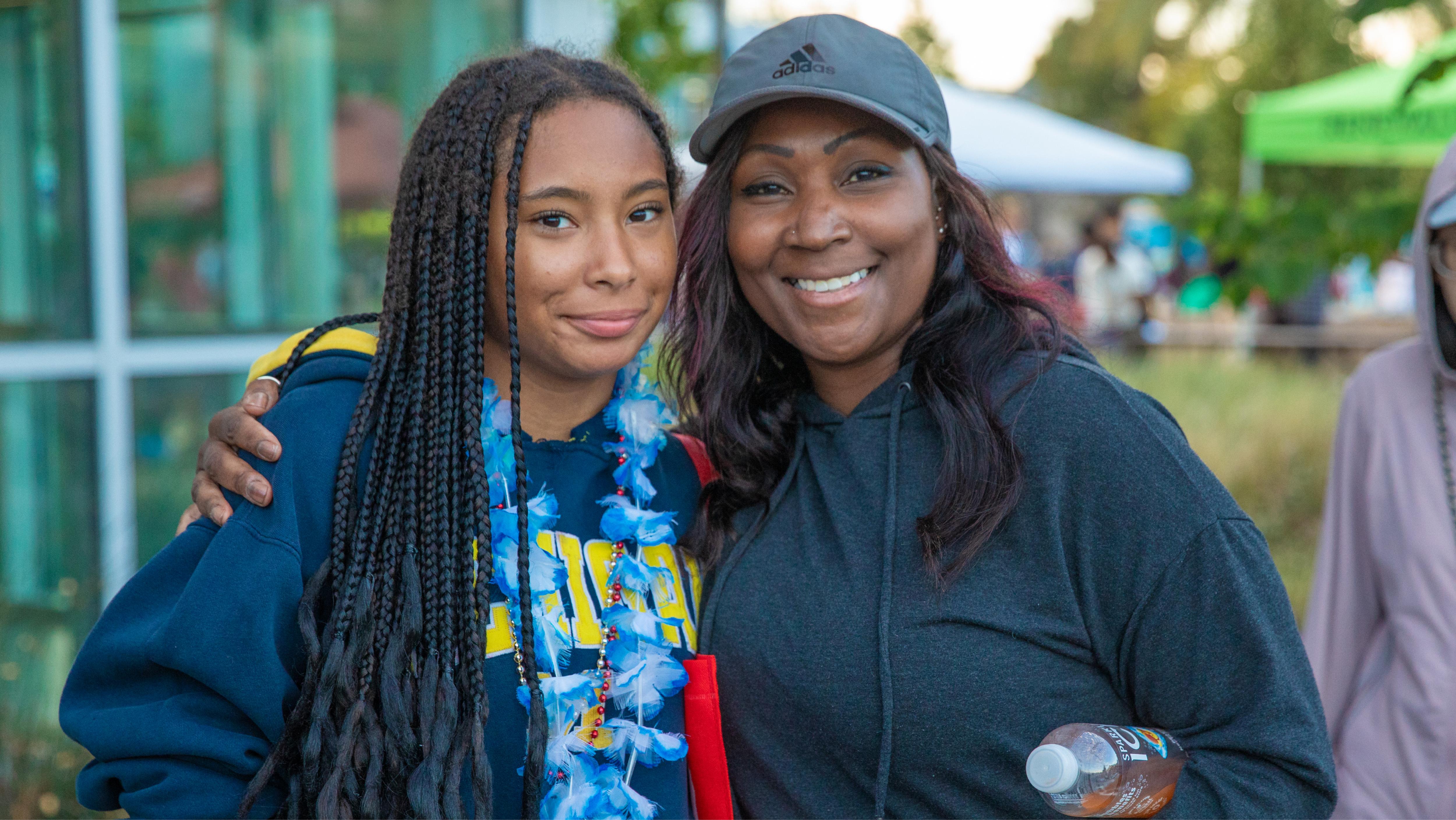 A student wearing a floral lei posing with a supportive family member at an outdoor campus celebration.