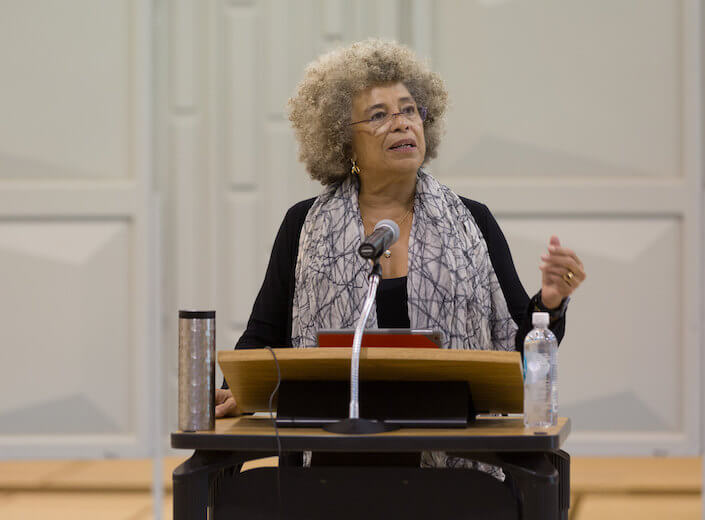 Angela Davis at a podium as she delivers a speech for students.