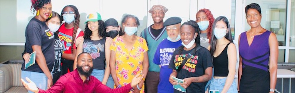 Group of Umoja students and faculty in a group, posing for a photo. Some are wearing paper face barroers, others are not. There are both male and female, young adult and older adults.