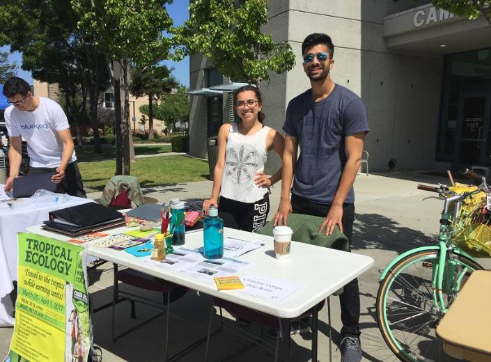 Two students, one male and one female stand a booth at an Eco Fair on campus.