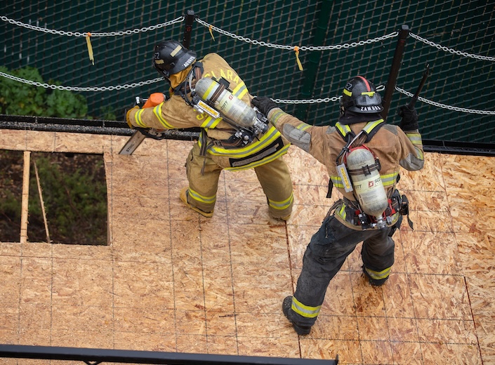 Group of firefighter cadets in gear at a drill. Four are men, one is a woman.