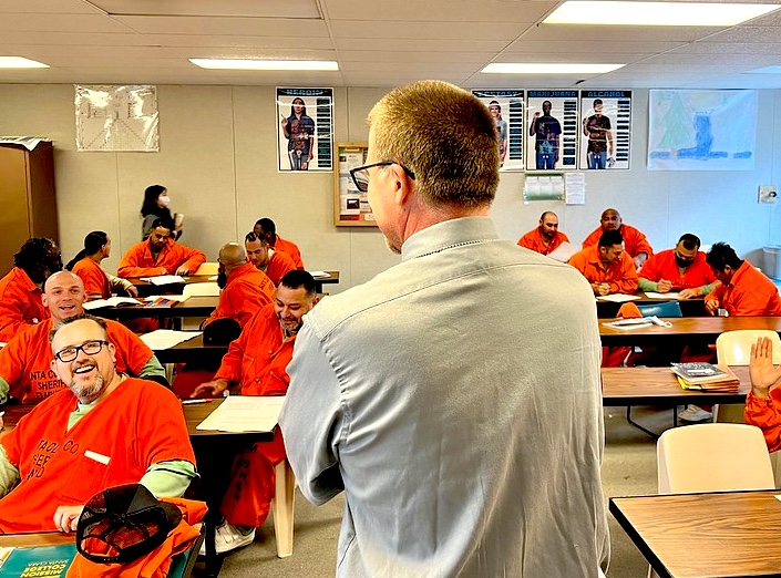 Jeff Cormier faces class of inmates in orange jumpsuits.